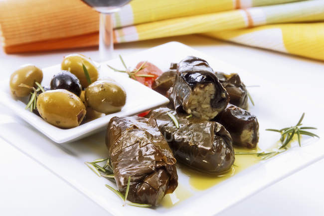 Stuffed vine leaves and olives on white plate — Stock Photo