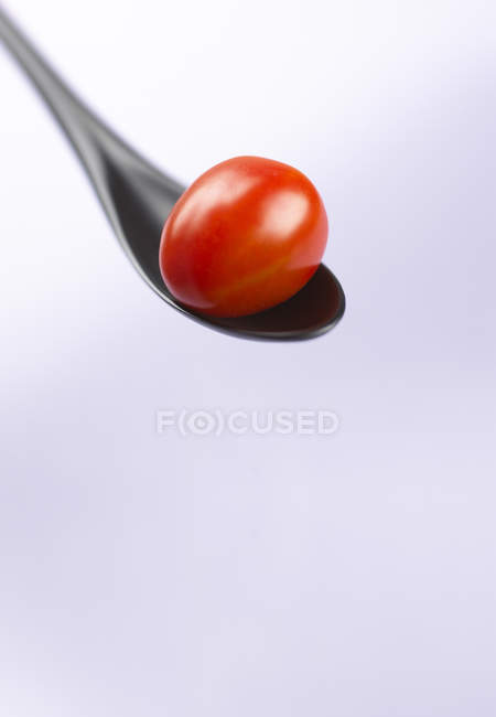 Red cocktail tomato on black spoon — Stock Photo