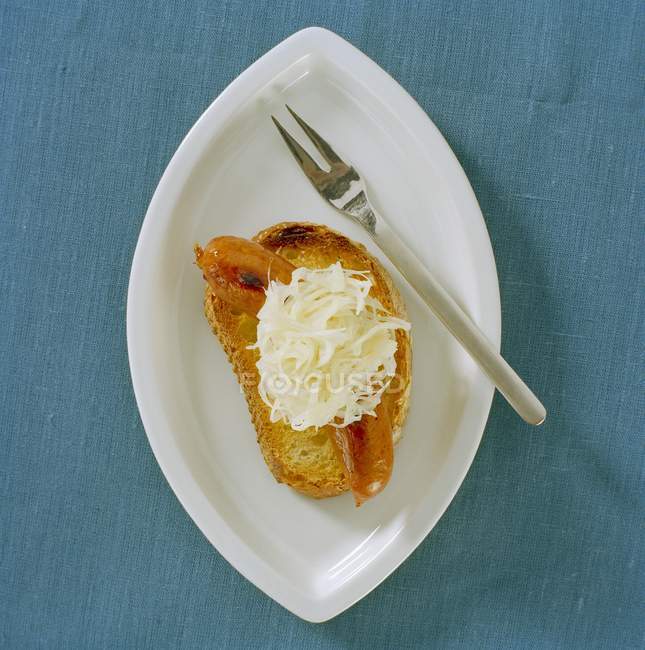 Salsicha com chucrute em fatia de pão torrado em placa branca com garfo — Fotografia de Stock