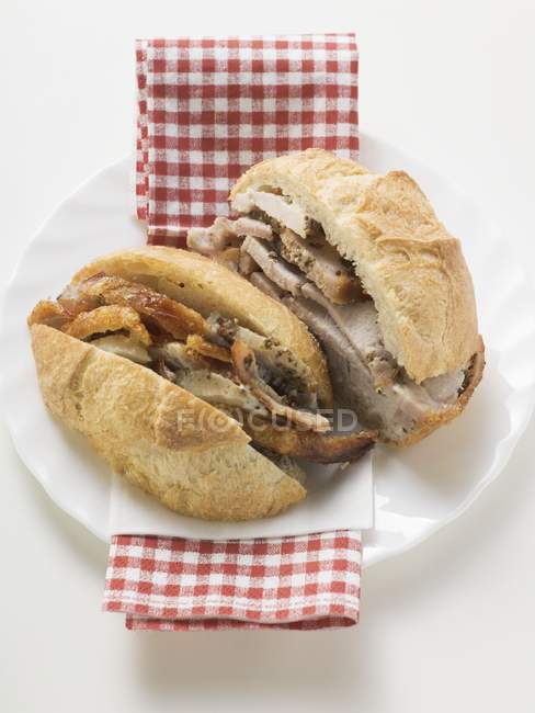 Primer plano de cerdo asado en rollo de pan, cortado a la mitad, en servilleta - foto de stock