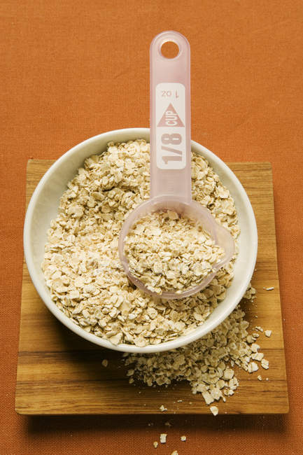 Rolled oats in a bowl with plastic measuring spoon — Stock Photo