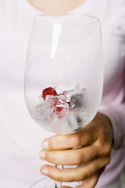 Primer plano vista recortada de la persona sosteniendo cubos de hielo de bayas en vidrio - foto de stock