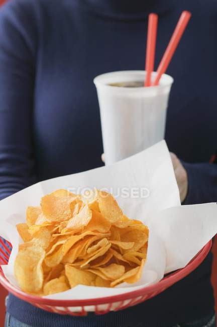 Woman holding basket of crisps and cola — Stock Photo