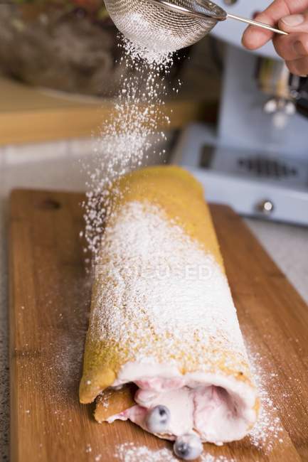 Cropped view of hand sprinkling sponge Roulade with icing sugar — Stock Photo