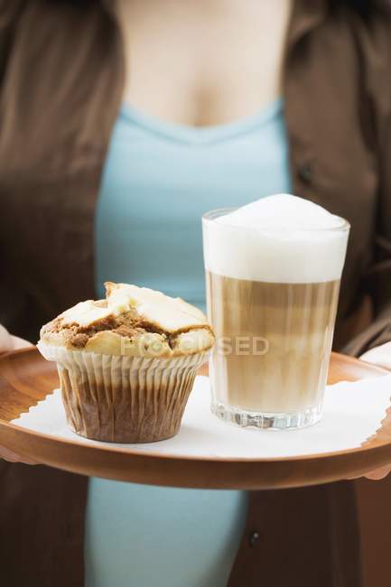 Mulher segurando bandeja com latte e muffin — Fotografia de Stock
