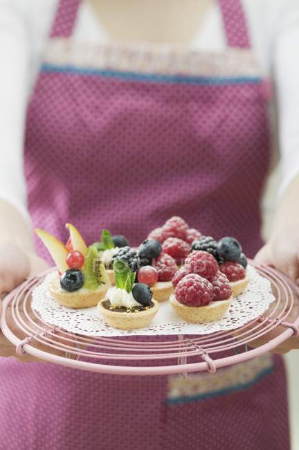 Closeup cropped view of woman in apron holding assorted berry tarts — Stock Photo