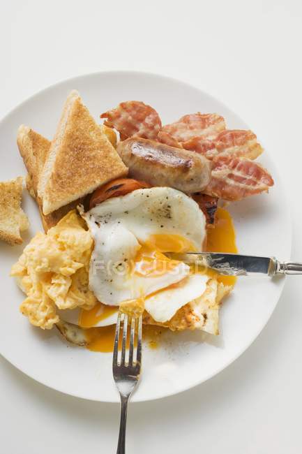 Вид зверху смаженого яйця з беконом, ковбасою і тостами на тарілці — стокове фото