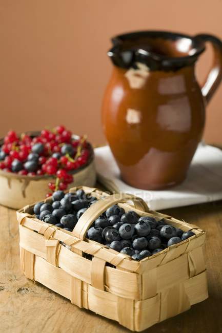 Blueberries in basket and bowl of berries — Stock Photo