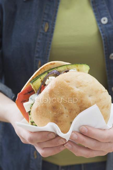 Closeup view of woman holding toasted roll filled with grilled vegetables — Stock Photo