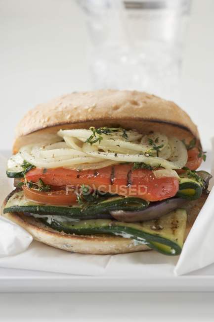 Toasted roll filled with grilled vegetables on white plate with paper — Stock Photo