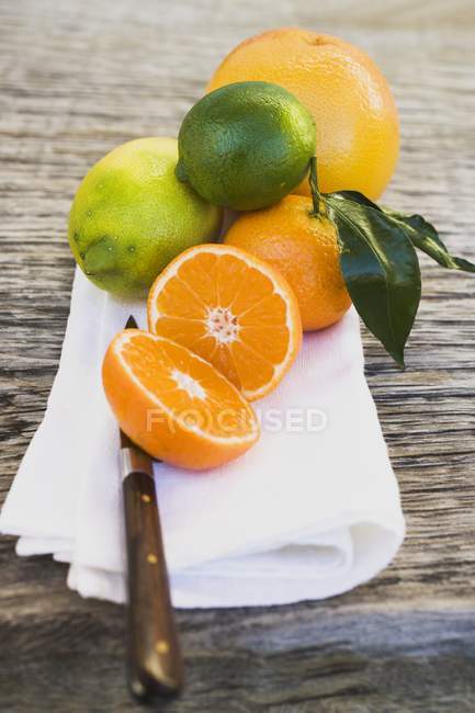 Closeup view of assorted citrus fruits on white cloth with knife on wooden background — Stock Photo