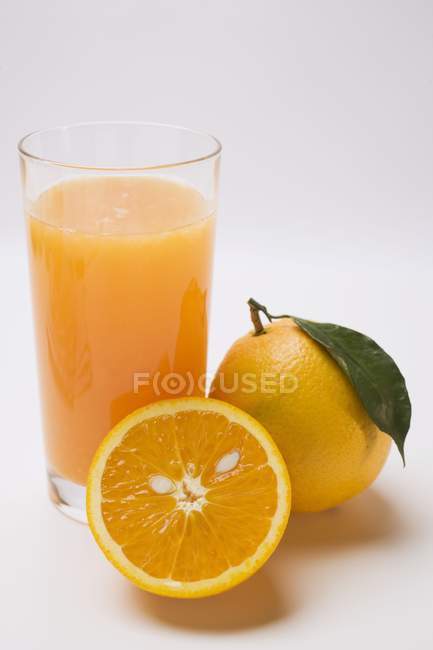 Vaso de zumo fresco y naranjas - foto de stock
