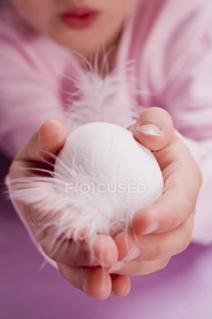 Cropped view of child holding a white egg with feathers — Stock Photo