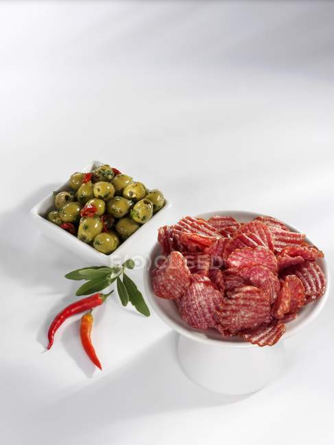 Slices of salami with green olives and chillies — Stock Photo