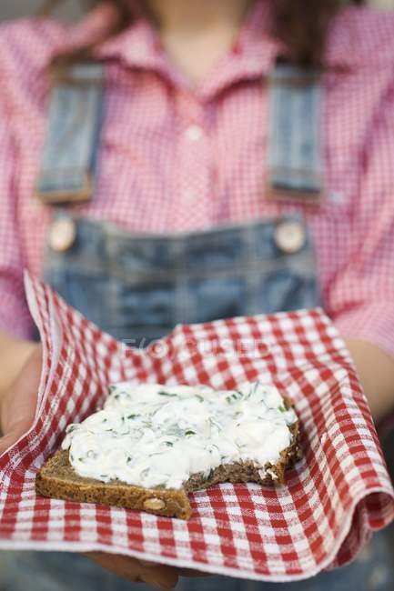 Woman holding wholemeal bread with quark and ramsons on napkin in hands, midsection — Stock Photo