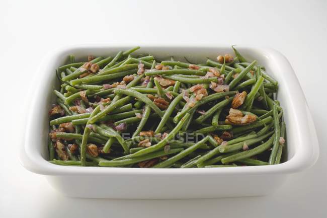 Green beans with bacon and pecans in white dish  on white background — Stock Photo