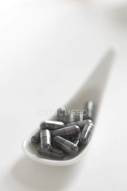 Vista de cerca de las cápsulas de carbón sobre una cuchara de porcelana - foto de stock