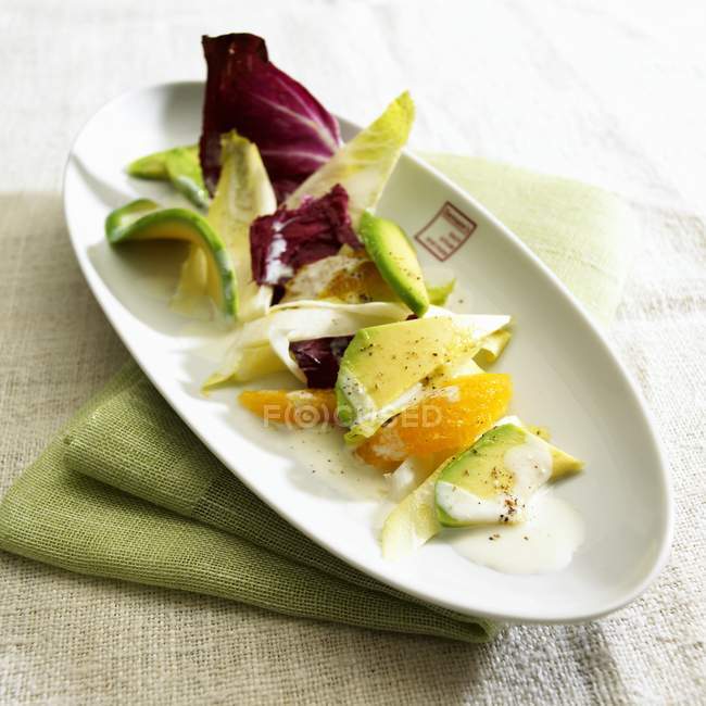 Салат з апельсином та авокадо на білій тарілці над зеленим рушником — стокове фото