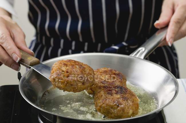 Closeup view of woman frying burgers in a frying pan — Stock Photo