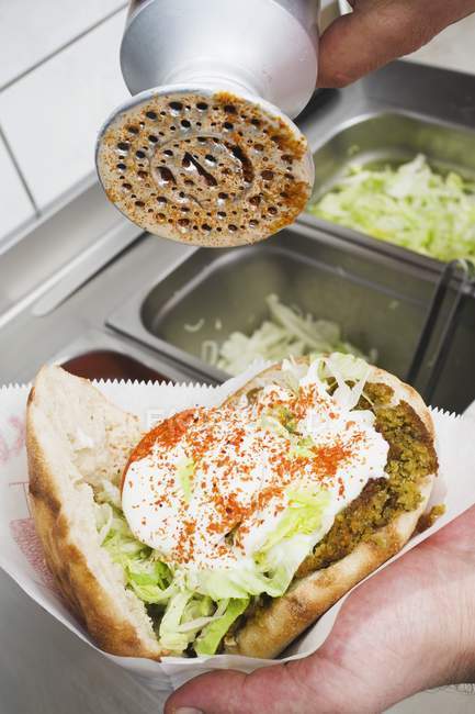 Ajouter un assaisonnement épicé à un kebab de dîner enveloppé dans du papier à la main — Photo de stock