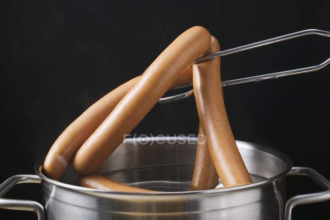 Lifting frankfurters out of a pan — Stock Photo