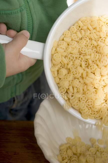 Child pouring wheel pasta into bowl — Stock Photo