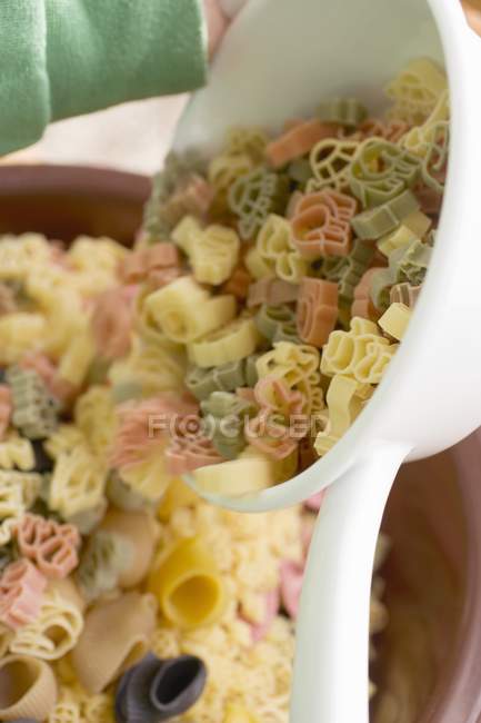 Coloured animal pasta pouring out of strainer — Stock Photo
