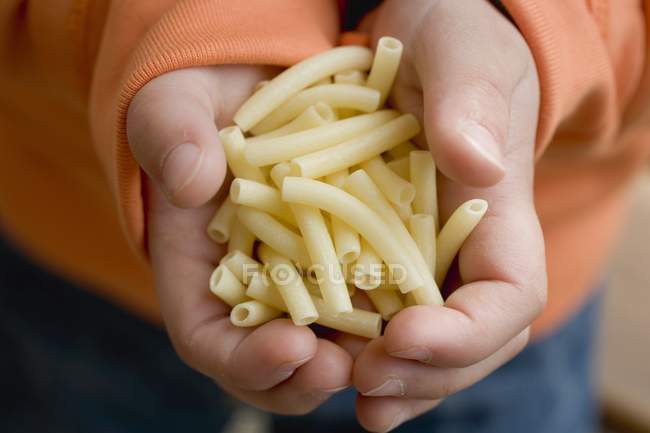 Child holding macaroni pasta — Stock Photo