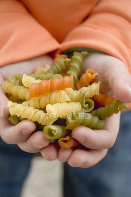 Criança segurando macarrão espiral colorido — Fotografia de Stock