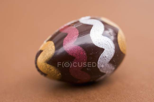 Vista de primer plano de huevo de chocolate pintado sobre fondo marrón - foto de stock