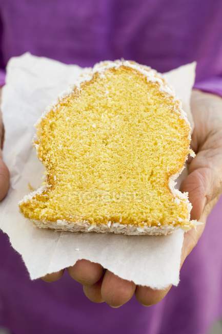 Обрезанный вид человека, держащего кусок сладкого пирога с кокосовыми хлопьями — стоковое фото
