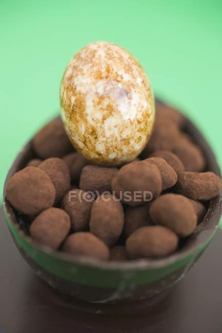 Крупним планом шоколадне яйце наполовину заповнене дрібними трюфелями та білим шоколадним яйцем — стокове фото