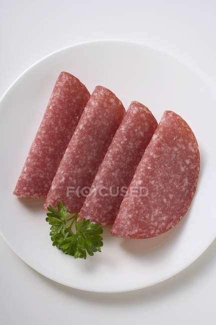 Four slices of salami with parsley — Stock Photo