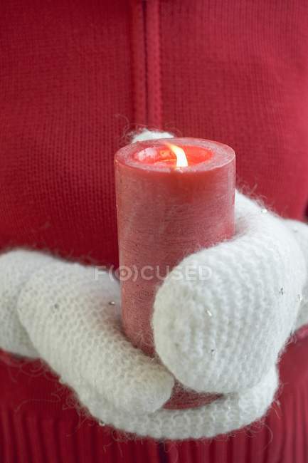 Vista de cerca de las manos en manoplas con vela roja encendida - foto de stock