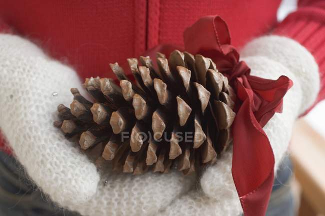 Closeup view of hands in mittens holding cone with red bow — Stock Photo