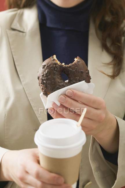 Woman holding doughnut and cup of coffee — Stock Photo