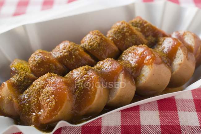 Closeup view of sliced Currywurst sausage with ketchup and curry powder in paper dish — Stock Photo