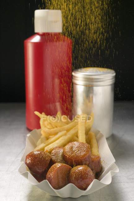 Curry powder pouring on currywurst and chips — Stock Photo
