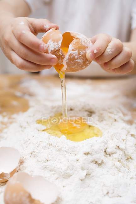 Ausgeschnittene Ansicht eines Kindes, das ein Ei auf einen Mehlhaufen bricht — Stockfoto