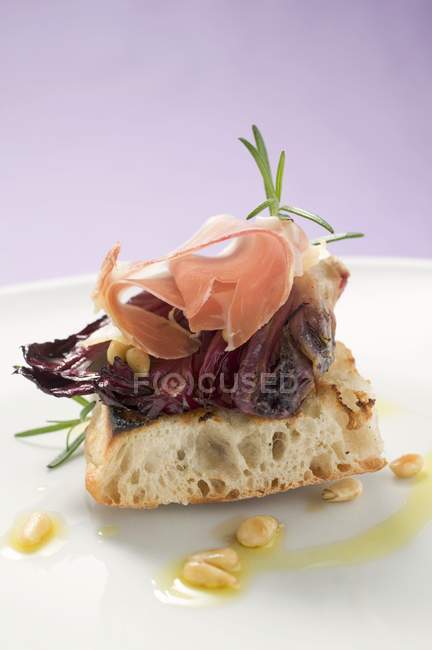 Flatbread topped with radicchio, Parma ham and pine nuts on white plate — Stock Photo