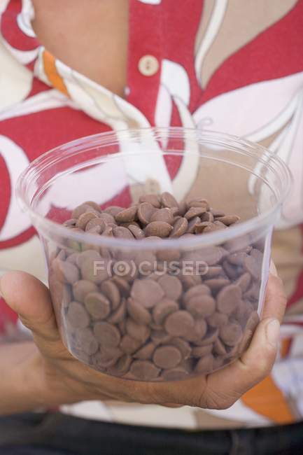 Closeup cropped view of woman holding tub of chocolate buttons — Stock Photo
