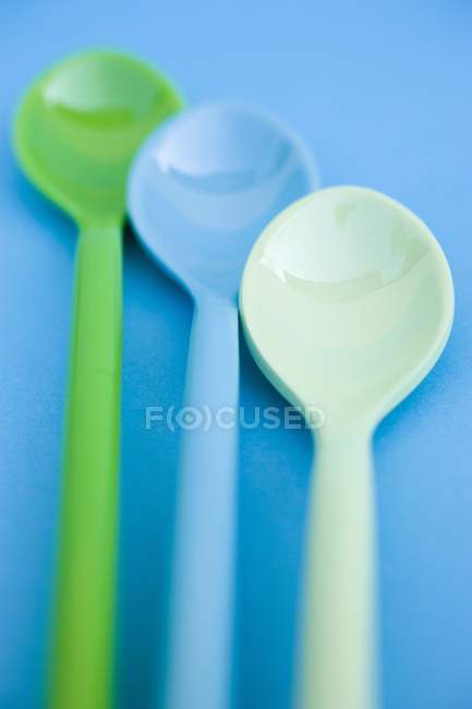 Primo piano vista di tre cucchiai di plastica colorata sulla superficie blu — Foto stock