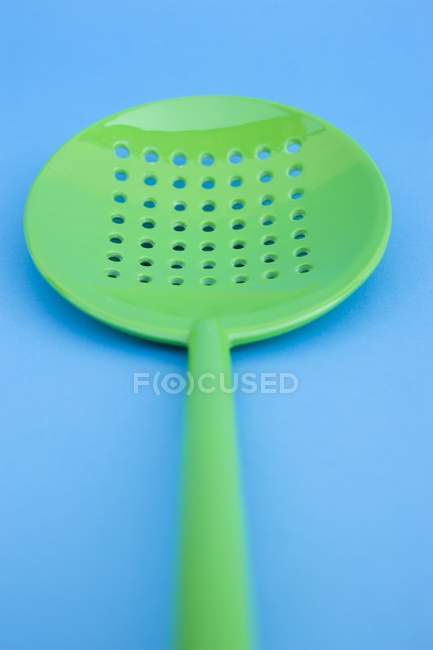 Closeup view of green slotted spoon on blue surface — Stock Photo