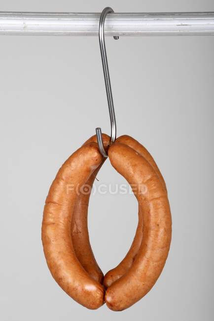 Closeup view of four red bratwurst sausages hanging on a hook — Stock Photo