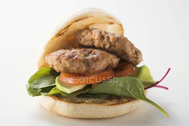 Meat patties with spinach and avocado in hamburger roll  laying on white surface — Stock Photo