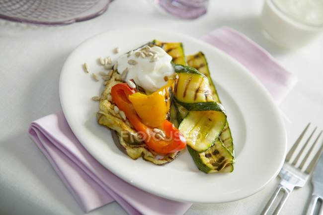 Grilled vegetables with crme frache and sunflower seeds on white plate over towel with fork — Stock Photo