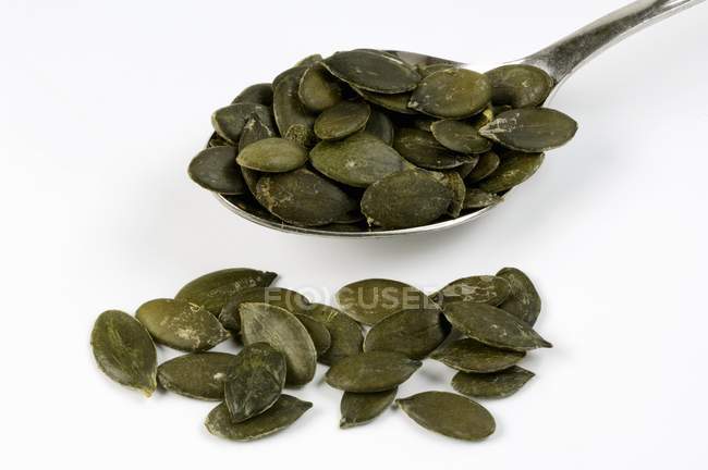 Closeup view of pumpkin seeds with spoon on white surface — Stock Photo