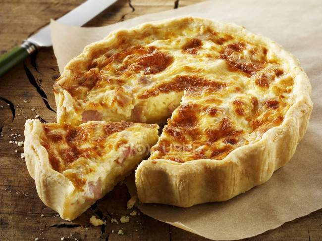 Closeup view of Quiche Lorraine with a cut slice on baking parchment — Stock Photo