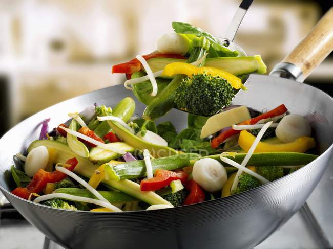 Verduras mixtas en wok y en espátula con fondo borroso - foto de stock