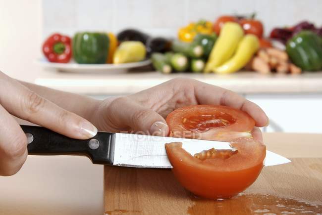 Hand Cutting up a tomato on wooden desk by knife — Stock Photo